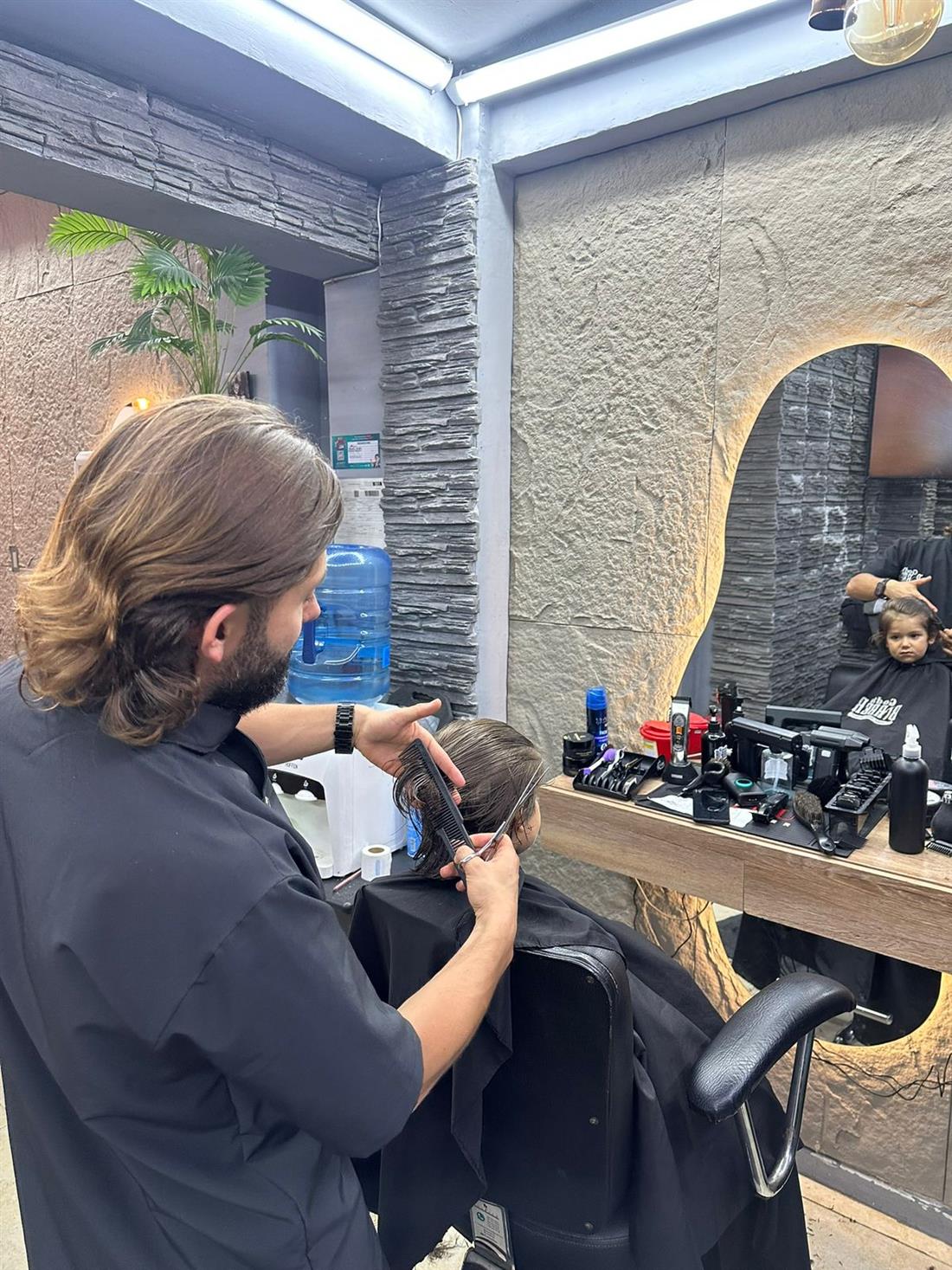 Barbero de God's Barber trabajando frente al espejo en arco con luz cálida